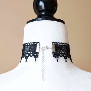 May include: Black lace choker necklace with a silver chain and adjustable clasp. The choker is made of delicate lace and has a scalloped edge.