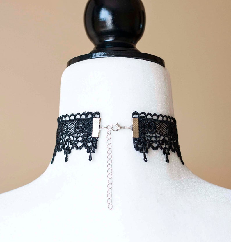 May include: Black lace choker necklace with a silver chain and adjustable clasp. The choker is made of delicate lace and has a scalloped edge.