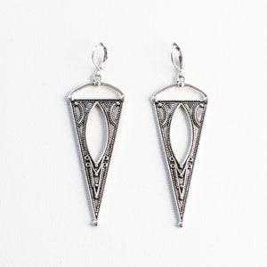 May include: A pair of silver dangle earrings with a geometric, triangular design. The earrings have a detailed, intricate pattern.