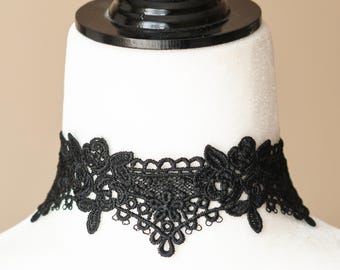May include: Black lace choker necklace with floral and geometric patterns. The choker is displayed on a white mannequin head. The lace design features intricate details and a delicate appearance, suitable for special occasions or everyday wear.
