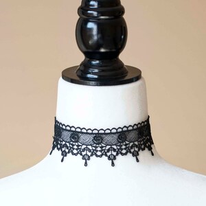 May include: A black lace choker necklace with a delicate floral design. The choker is displayed on a white mannequin bust.