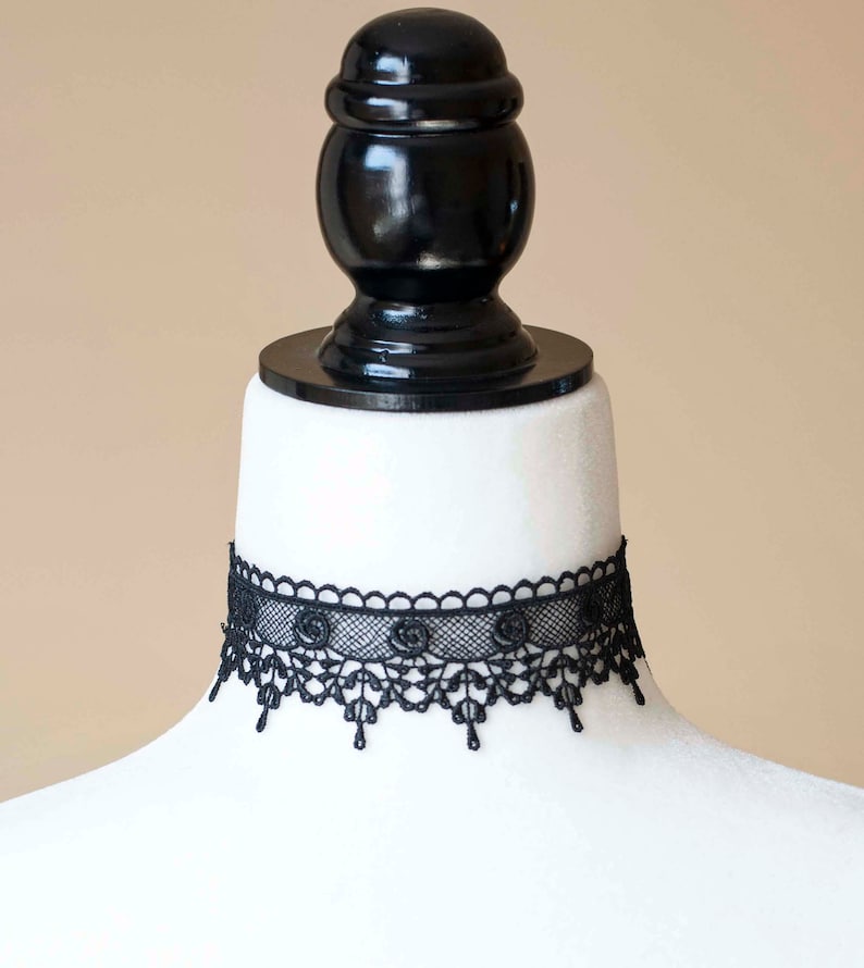 May include: A black lace choker necklace with a delicate floral design. The choker is displayed on a white mannequin bust.
