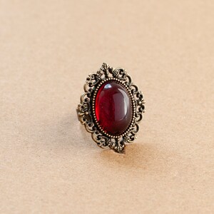 May include: A red gemstone ring with an ornate gold setting. The ring has a detailed design with intricate swirls and curves.