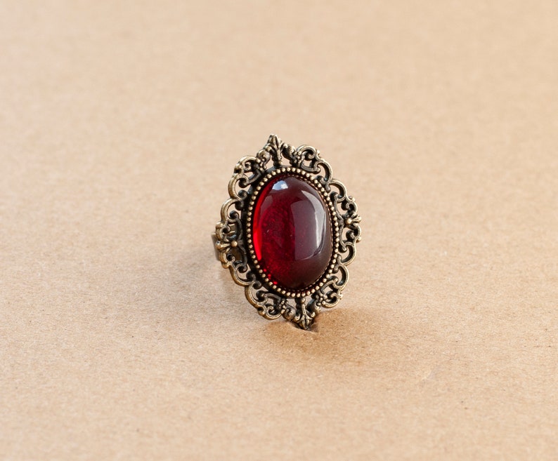 May include: A red gemstone ring with an ornate gold setting. The ring has a detailed design with intricate swirls and curves.