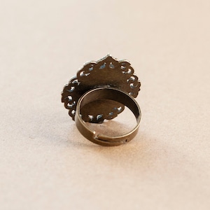 May include: A gold-toned ring with a filigree design. The ring is open in the back and has a simple band.
