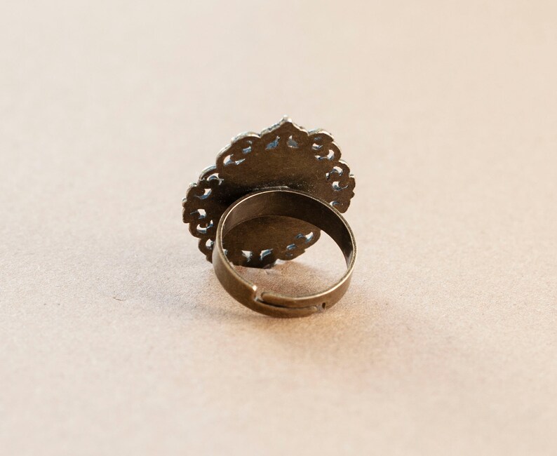 May include: A gold-toned ring with a filigree design. The ring is open in the back and has a simple band.