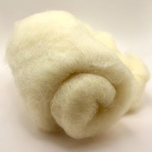 May include: A close-up of a pile of soft, off-white wool roving. The wool is tightly packed and has a fluffy, textured appearance. The fibers are fine and appear to be natural. This wool is suitable for various fiber art projects.