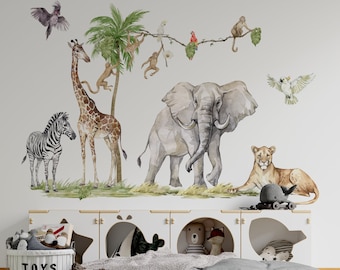 May include: A white wall with a jungle animal themed wall decal featuring a giraffe, zebra, elephant, lion, monkeys, and birds. The decal is above a white shelf with a gray and white blanket and a blue whale toy.