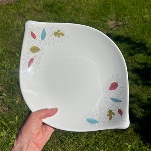 May include: White, leaf-decorated serving platter. The platter has a unique, curved shape and is adorned with colorful leaf designs in red, blue, and green. The leaves are set against a white background, creating a vintage aesthetic.