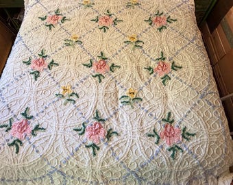 May include: A white chenille bedspread featuring a raised diamond lattice pattern with light blue accents. The design is decorated with tufted pink rose motifs and smaller yellow flower clusters, each accompanied by green leaves and stems.
