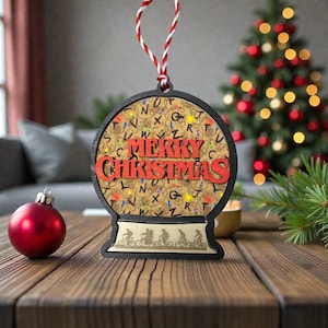 May include: A wooden Christmas ornament in the shape of a snow globe. The ornament features the words "MERRY CHRISTMAS" in red, with a background of lights and letters. A red and white string is attached for hanging.