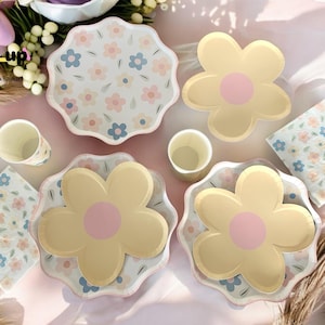 May include: A set of pastel floral themed paper plates and napkins. The plates feature a large yellow flower with a pink center and a smaller floral pattern. The napkins feature a smaller floral pattern in pink, blue, and yellow.