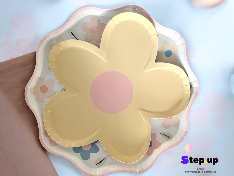 May include: A yellow and pink flower-shaped paper plate with a scalloped edge. The plate has a floral pattern with pink, yellow, and blue flowers.