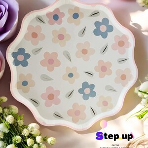 May include: White paper party plates with a pink, blue and beige floral pattern. The plates have a scalloped edge and are ideal for a spring or summer party.