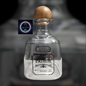 May include: A clear glass bottle of Patron Silver Tequila with a wooden top. The bottle has a label that says "Tequila 100% de Agave" and "Silver Patron". The label also says "Hecho en Mexico" and "Made in Mexico".