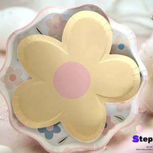 May include: A yellow flower-shaped paper plate with a pink centre. The plate has a white scalloped edge and a floral pattern.