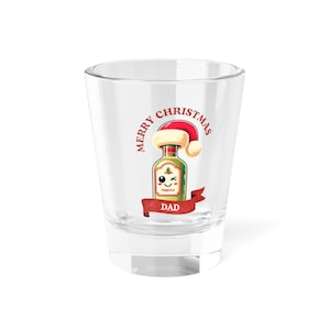 May include: A clear shot glass with a festive design. The glass features a cartoon tequila bottle wearing a Santa hat, with the words "Merry Christmas Dad" in red. The bottle has a winking face and is set against a white background.