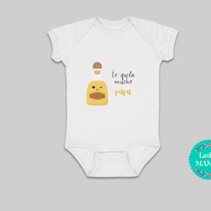 May include: White baby bodysuit featuring a cartoon tequila bottle with a smiling face. The text "Te quila mucho papa" is in black and yellow. A Latina Mamas logo is in the bottom right corner of the image.