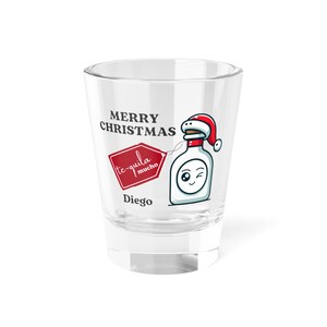 May include: Clear shot glass featuring a cartoon tequila bottle wearing a Santa hat. The glass is printed with "Merry Christmas" and "te-quila mucho" in a red diamond. The name "Diego" is also printed on the glass.