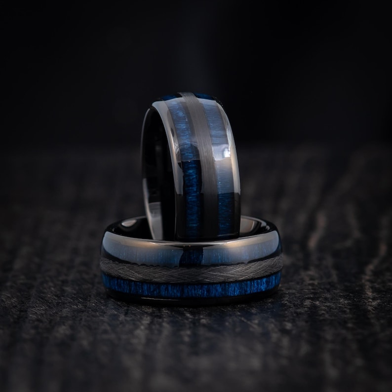 May include: Two black tungsten carbide rings with blue inlay. The rings are stacked on top of each other.