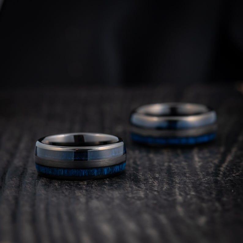 May include: Two black and blue tungsten carbide rings with a brushed finish. The rings have a blue inlay and are stacked on top of each other.