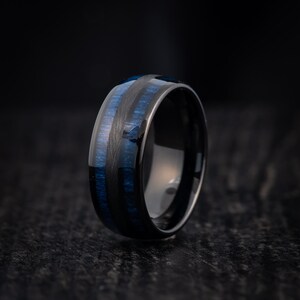 May include: A black tungsten carbide ring with blue wood inlay. The ring has a polished finish and a comfortable fit.
