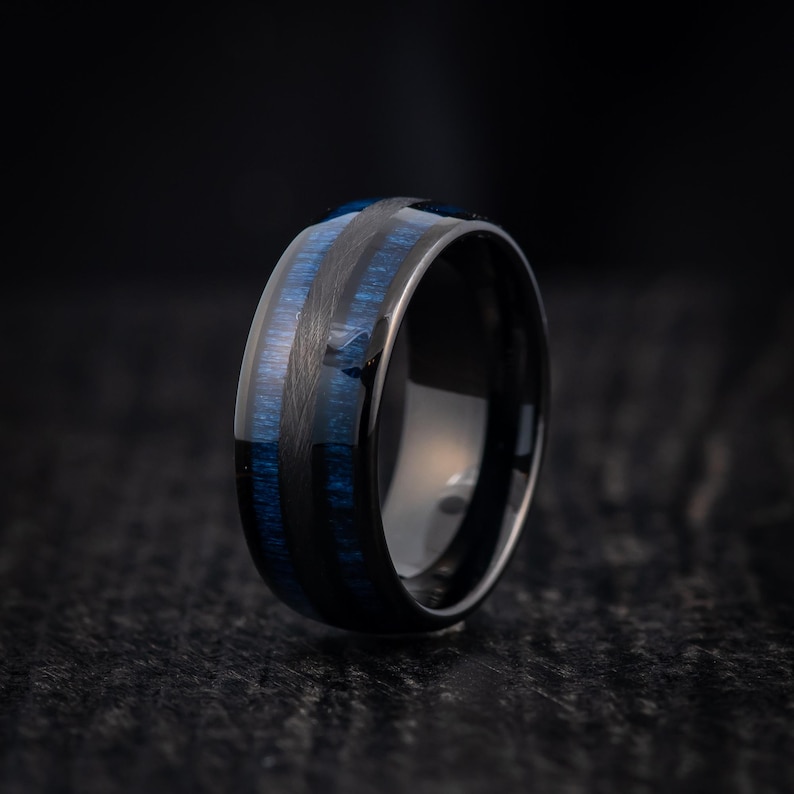 May include: A black tungsten carbide ring with blue wood inlay. The ring has a polished finish and a comfortable fit.