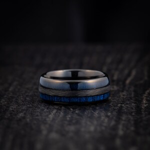 May include: A black and blue ring with a dark blue inlay. The ring is made of tungsten carbide and has a polished finish.