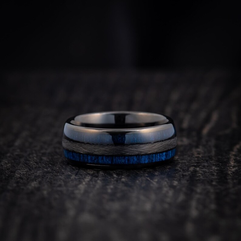 May include: A black and blue ring with a dark blue inlay. The ring is made of tungsten carbide and has a polished finish.