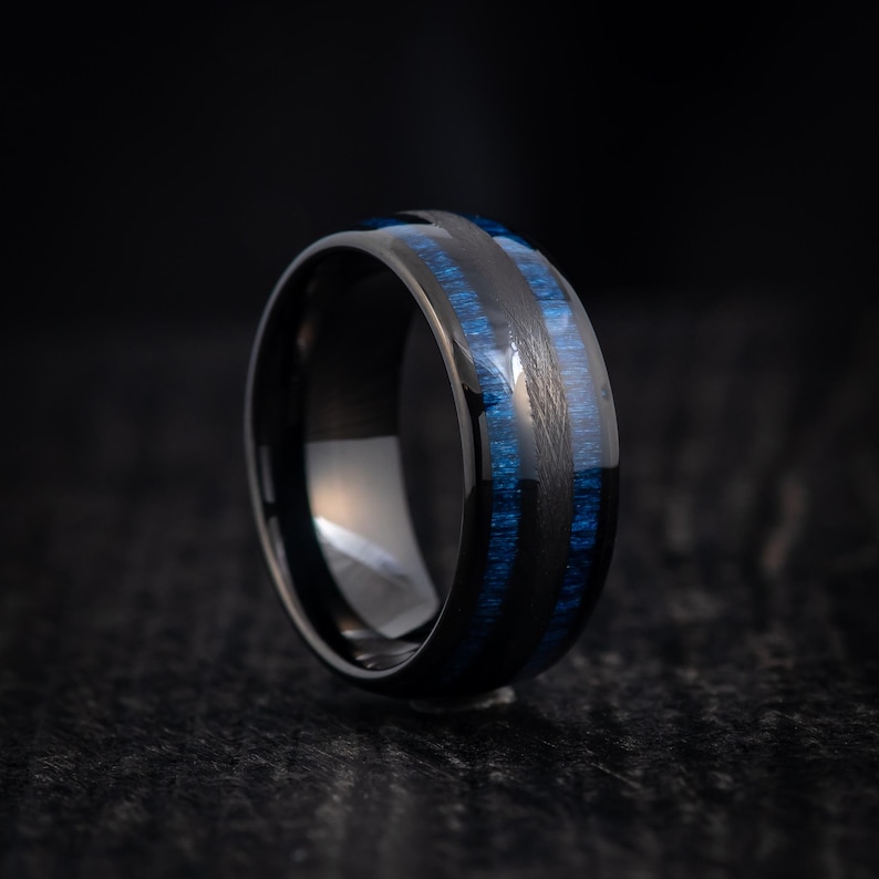 May include: A black tungsten carbide ring with blue wood inlay. The ring has a polished finish and a comfortable fit.