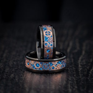 May include: Two black and rose gold rings with blue and rose gold gear designs. The rings are stacked on top of each other.