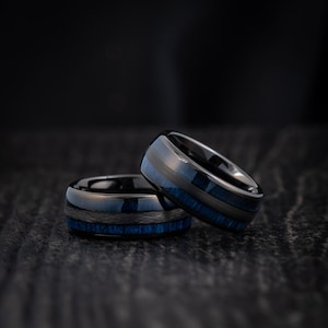 May include: Two black tungsten carbide rings with blue inlay. The rings are stacked on top of each other.