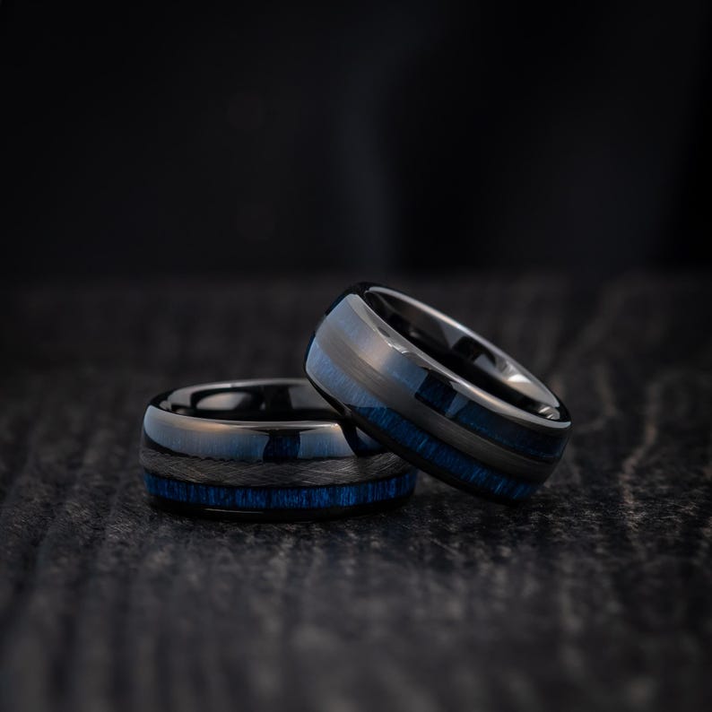May include: Two black tungsten carbide rings with blue inlay. The rings are stacked on top of each other.