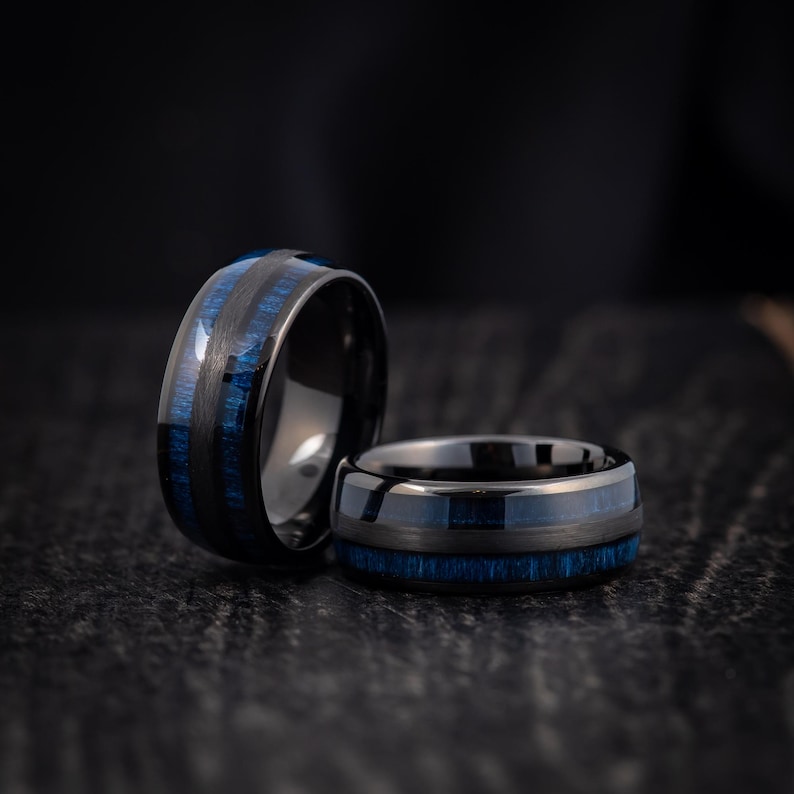 May include: Two black tungsten carbide rings with blue wood inlay. The rings are stacked on top of each other.