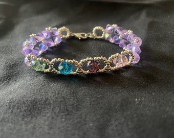May include: A delicate bracelet with a silver chain and purple, blue, and green crystal beads.