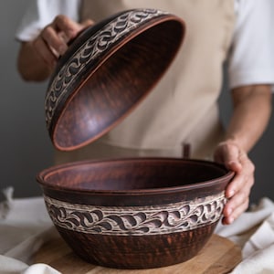 Könnte beinhalten: Eine braune Brot-Glocke aus Keramik mit Deckel, verziert mit einem dekorativen Blumenmuster. Die Glocke ist geöffnet und zeigt das Innere.