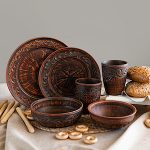 Könnte beinhalten: Ein rustikales, braunes Keramik-Geschirrset mit Tellern, Schalen und Tassen. Die Teller und Tassen haben ein dekoratives Blumenmuster an den Rändern. Brot und Brotstangen sind ebenfalls zu sehen.