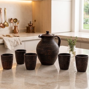 May include: A dark brown ceramic pitcher with a rounded body and a matching handle, accompanied by four matching cylindrical cups. Each piece features an intricate, embossed swirling pattern across the surface, showcasing a textured, rustic finish.