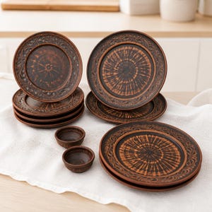 May include: A set of dark brown ceramic plates and two small bowls featuring a central sunburst pattern and an embossed floral border. The plates are stacked in three groups, showcasing a consistent rustic finish with dark and light brown tones.