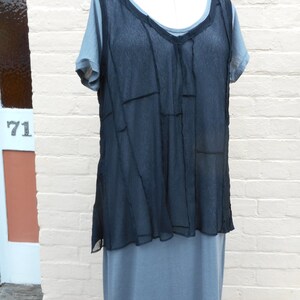 以下が含まれることがあります： 重ね着の切り替えデザインが施された黒いシアーなトップス。グレーのノースリーブドレスの上に重ねて着ています。