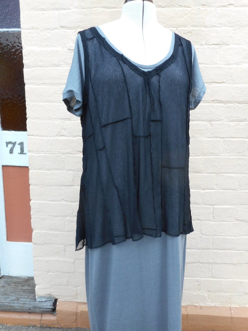 以下が含まれることがあります： 重ね着の切り替えデザインが施された黒いシアーなトップス。グレーのノースリーブドレスの上に重ねて着ています。