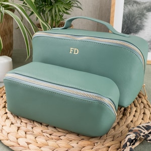 May include: Two green zippered cosmetic bags. The larger bag has a gold zipper and the initials "FD" in gold lettering. The smaller bag has a silver zipper.