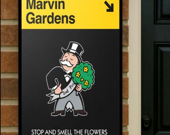May include: A black sign with yellow top section that reads "Marvin Gardens" with an arrow. Below is a cartoon of a Monopoly man holding flowers, with the text "2nd Prize". The bottom of the sign reads "STOP AND SMELL THE FLOWERS".