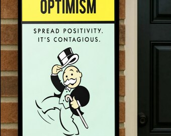 May include: A framed sign with the word "OPTIMISM" in bold black letters on a yellow background. Below, the sign reads "SPREAD POSITIVITY. IT'S CONTAGIOUS." A cartoon figure in a tuxedo and top hat is depicted on a light green background.