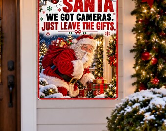 May include: A rectangular metal sign featuring a security camera icon and the text SANTA WE GOT CAMERAS. JUST LEAVE THE GIFTS. The image shows Santa Claus with a red sack and wrapped presents, surrounded by green snowflakes on a white background.