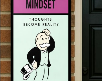 May include: A framed sign with the word "MINDSET" in white on a pink background. Below, the text "THOUGHTS BECOME REALITY" is displayed above a cartoon illustration of a man in a suit and top hat.