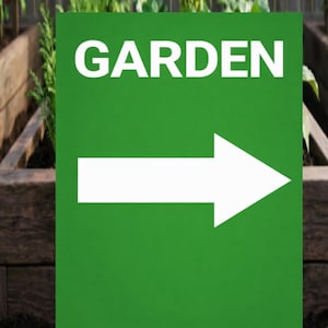 May include: A green rectangular sign with the word "GARDEN" in white capital letters and a white arrow pointing right. The sign is set against a background of wooden garden beds.