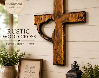 May include: A rustic wooden cross with a heart-shaped cutout, mounted on a white-painted wall. The cross is made of dark brown wood and features the text "RUSTIC WOOD CROSS" and "FAITH • HOPE • LOVE". A framed print with the text "Be still and know" is also visible.