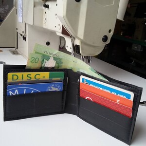 Puede incluir: Una cartera negra hecha de c&aacute;maras de aire de neum&aacute;ticos recicladas, abierta para revelar varias tarjetas y billetes canadienses. La cartera tiene una superficie texturizada y est&aacute; sobre una superficie blanca.