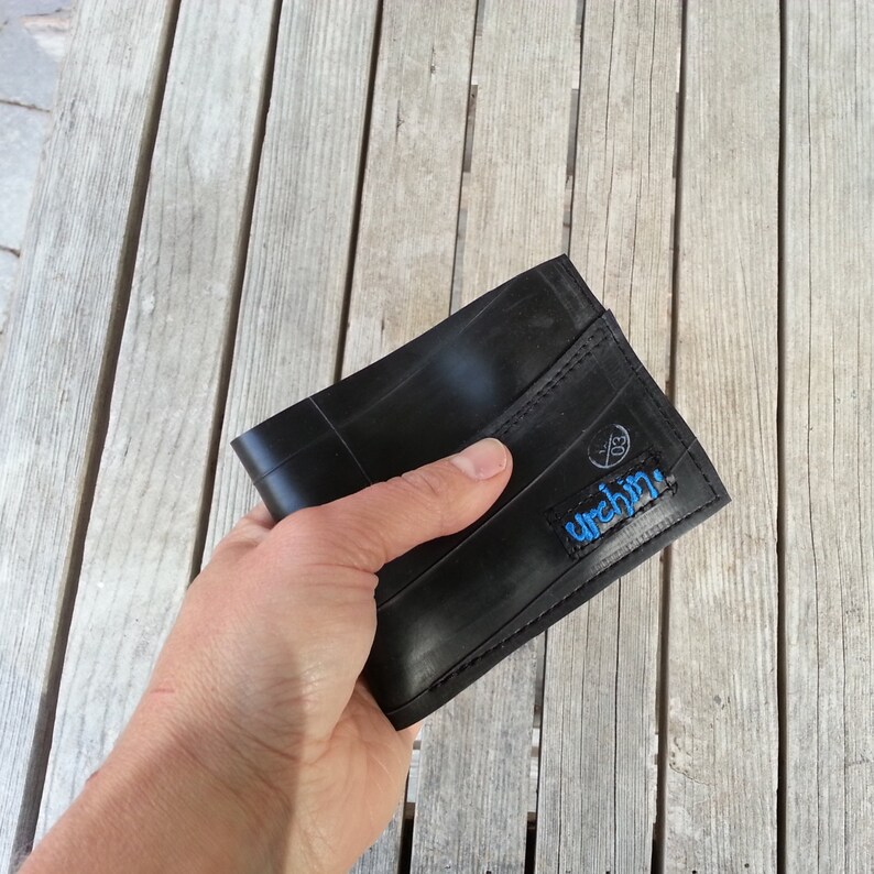 Puede incluir: Una cartera de cuero negro hecha de c&aacute;maras de bicicleta recicladas. La cartera tiene un logotipo azul cosido que dice "urchin".